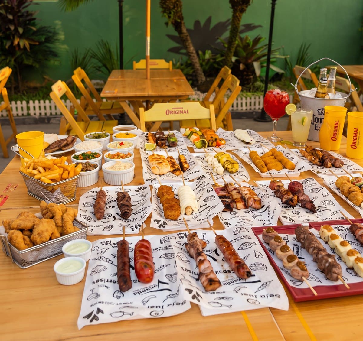 Mesa comprida com espetos, porções e molhos, pronta para um aniversário